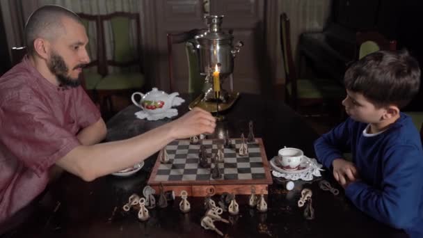 Вид збоку милий маленький 6s син і молодий батько грають в шахи сидячи в приміщенні . — стокове відео