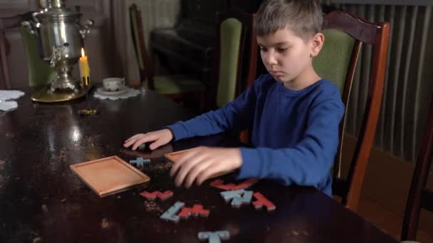 Chłopiec zbiera puzzle siedząc przy stole — Wideo stockowe