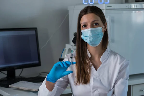 Tıbbi maskeli ve eldivenli kadın doktor kapağı çıkararak enjeksiyon için önceden doldurulmuş şırıngayı hazırlıyor.