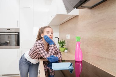 Yorgun genç bir temizlikçi evi temizledikten sonra mutfakta dinlenir, mutfak tezgahına yaslanır. Genç bir kız düşünceli bir şekilde koruyucu eldivenlerle mutfakta durur..
