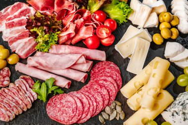 Lezzetli peynirler ve soğuk pirzolalarla dolu köy ahşap bir masanın üst görüntüsü. Zeytin, üzüm ve fındık gibi bazı meyveler kompozisyonu tamamlar..