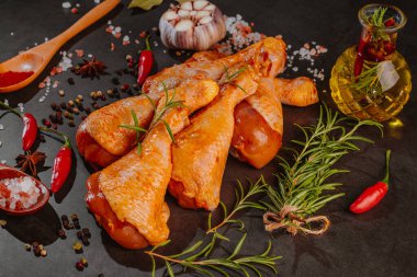 Kırmızı biber, biberiye ve baharatlı koyu bir arka planda tavuk budu..