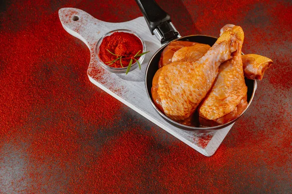 Chicken drumstick marinated in baking pan on a wooden background with spices, red hot pepper.