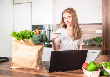 Yemek teslimatı, kendini izole etme konseptinde. Mutfak masasında yiyecek paketi olan bir kız. Kız yemek siparişi verdi..