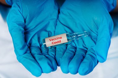 Aşı konsepti. Ulusun sağlığı. Elleri koruyucu kauçuk mavi eldivenler virüse karşı aşıyı tutuyor..