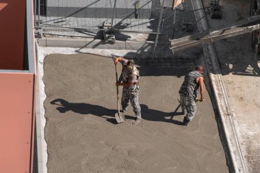 İki adam kaldırıma beton döşüyorlar. Yenileme çalışmaları.