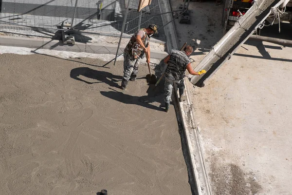 İki adam kaldırıma beton döşüyorlar. Yenileme çalışmaları.