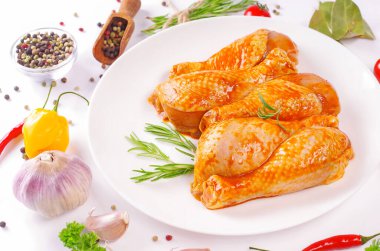 Terbiye edilmiş tavuk çubuğu beyaz bir tabakta ve pişirmek için baharatlar..