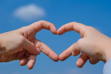 Gökyüzünde kalp şeklinde bir siluet oluşturan iki el