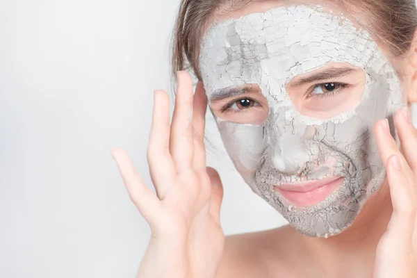 Beauty procedures skin care concept. Young woman applying facial gray mud clay mask to her face