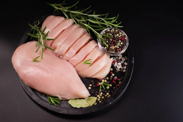Culinary gastronomy cooking background.Raw chicken meat slices on black background. Thinly sliced chicken fillet with rosemary. Diet food.