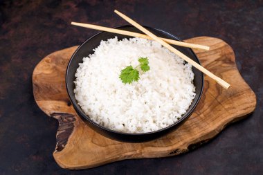 Ahşap bir mutfak tahtasının üzerinde yemek çubukları olan bir tabak pirinç. Bir porsiyon pirinç. Arka planda bir kase pirinç ve çubuk.