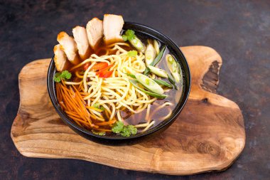 Tavuklu Çin eriştesi, siyah arka planda sebzeler. Mutfak tahtasındaki siyah kasede et ve sebzeli Çin eriştesi..