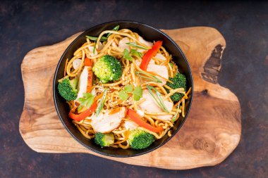 Çin eriştesi, et ve sebze parçaları. Mutfak tahtasındaki siyah kasede. Kızarmış Çin eriştesi, tavuk, sebze..