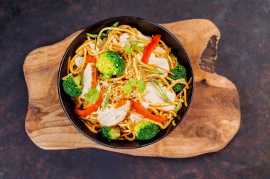 Tavuklu Çin eriştesi, siyah arka planda sebzeler. Mutfak tahtasındaki siyah kasede et ve sebzeli Çin eriştesi..