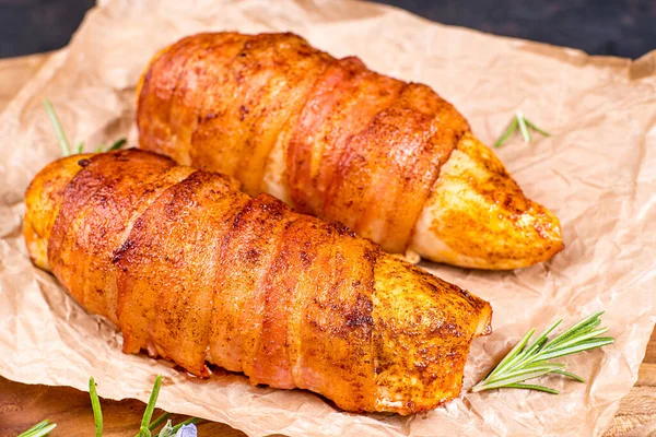 Chicken fillet wrapped with bacon slices on a wooden kitchen board on a blue background. Cooked chicken fillet in bacon.Baked chicken fillet wrapped in bacon, stuffed with cheese