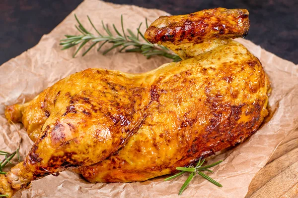 Grilled chicken . Half of baked chicken on food paper on a kitchen wooden board with spices and baked garlic.close-up