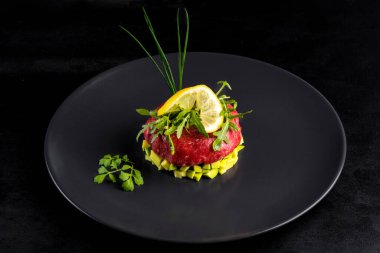 Siyah taş tabakta servis edilen yumurtalı biftek tartartarı. Avokado, otlar, tuz ve tavuk sarısı ile siyah bir tabakta tartar. Çiğ tarçınlı et. Siyah arka plan. Üst görünüm.