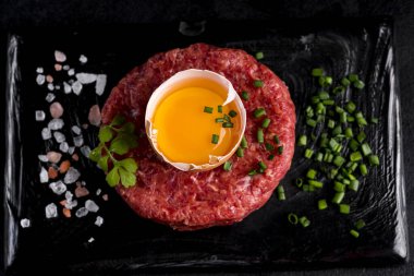 Siyah taş tabakta servis edilen yumurtalı biftek tartartarı. Siyah bir tabakta tart, otlar, tuz ve tavuk sarısı. Çiğ tarçınlı et. Siyah arka plan. Üst görünüm.