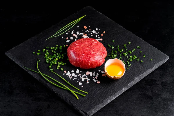 Beef tartar with egg served on a black stone plate. Tartar on a black plate with herbs, salt and chicken yolk. Raw tartare meat.Black background. Top view.