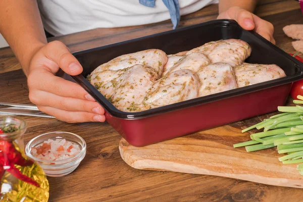 Marinated raw chicken wings for baking in the oven. Convenience food, precooked.The girl holds a tray with wings for baking in her hands, vegetables lie next to the table.
