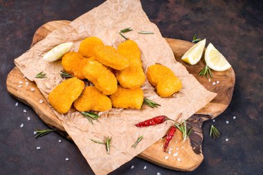 Ahşap mutfak tahtasının üzerinde kırmızı biber ve limon dilimleri ile haşlanmış nugget. Uygun yemek, hazır yemek. Fast food. Tahta kesim tahtasının üzerinde çeşitli tavuk nuggetları..