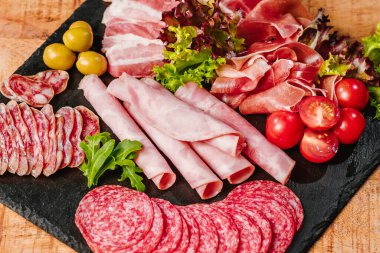 Sebzeli ahşap bir masada, siyah düz bir tabakta farklı türde sosis. Ahşap masada farklı sosisler servis ediliyor..