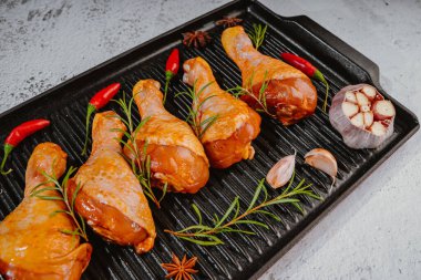 Baharat serpiştirilmiş çiğ tavuk budu, acı biber parçaları, körfez yaprakları tepeden görülmek üzere bir tabakta pişirilmeye hazır. Izgara tavasında baharatlı çubuk. Çiğ terbiye edilmiş tavuk eti. Çiğ but. Çiğ terbiye edilmiş tavuk eti. Ham davullar