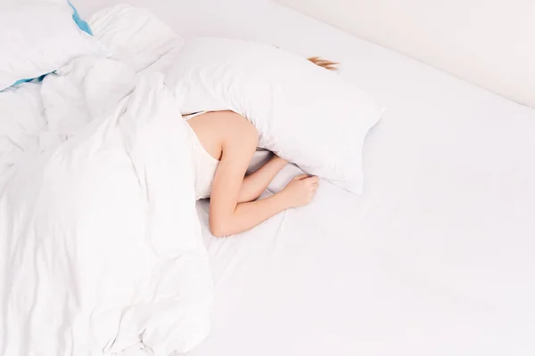 Sleep, early morning, waking up, noisy neighbors interfere, lack of sleep, too lazy to get out of bed. Young caucasian woman sleeps covering her head with pillows.