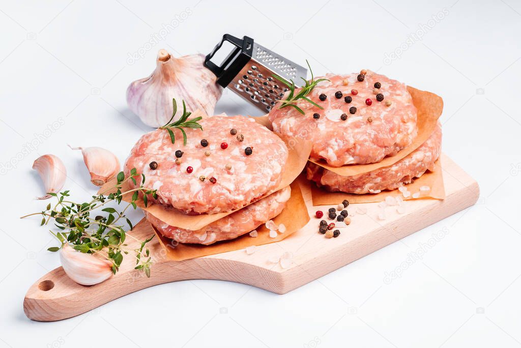Raw chicken burger on a white plate in a rosemary branch and spices. Instant meat. Grilled hamburgers.Raw Hamburger, meatballs on white background.Fast food at home.Convenience food, precooked.