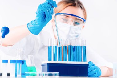 Koruyucu gözlüklü ve maskeli profesyonel kadın bilim adamı laboratuvarda reaktörlerle deney yapıyor. Reçeteli ilaç üretimi. Coronavirus salgını durması. Tıp konsepti