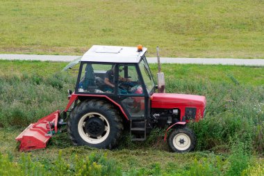 Römorklu traktör çim biçiyor. Çim biçme makinesine biniyor. Traktör şehirde çim biçiyor..