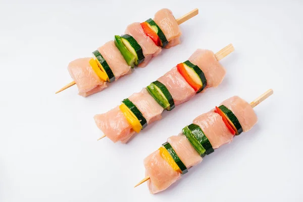 Three skewers strung with chicken fillet pieces with zucchini vegetables and bell peppers.Chicken skewers of kebab with vegetables, peppers and zucchini. isolade.