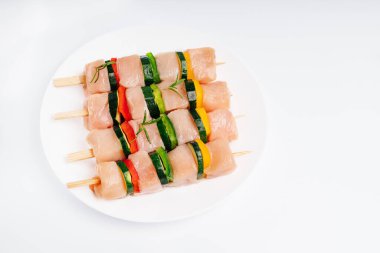 Beyaz bir arka planda, kabak sebzeli dört parça tavuk fileto ve dolmalık biberli dört şişe. Sebzeli tavuk kebabı, biber ve kabak..