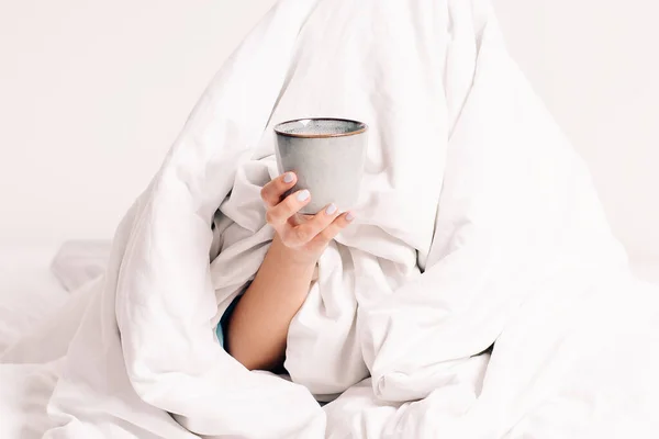 Young girl wrapped in a white blanket with her head does not want to get out of bed early in the morning.Concept of late,early waking up,headache early in morning.No desire to go to work ,bed rest.