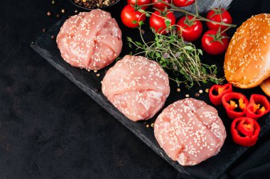 Uzayı kopyala Pastırmaya sarılmış üç tavuk burger, biberiye filizi, kırmızı biber, kiraz domatesleri ve siyah arka planda bir hamburger ekmeği. Fast food. Uygun yemekler, hızlı ev yemekleri..