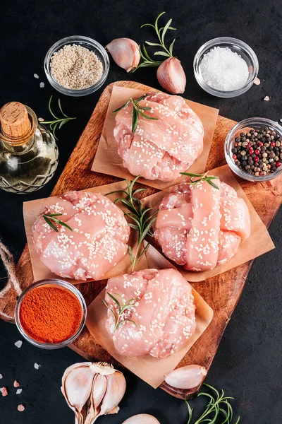 Close-up top view of four chicken burgers with rosemary branch with different spices to choose from for cooking on a black background. Fast food. Convenience food, fast home cooking.