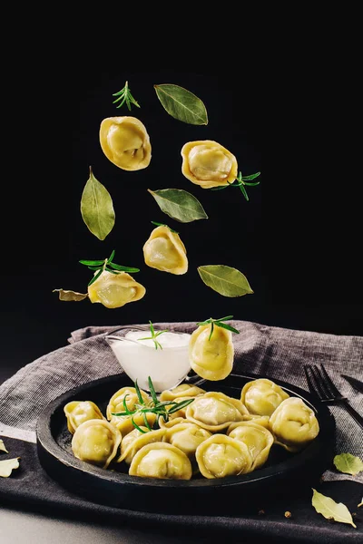 Food levitation.Dumplings with meat fly into the plate on a black background.