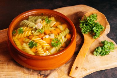 Erişte ve sebzeli tavuk çorbası. Makarna ve otlu tavuk çorbası. Koyu arkaplanda tahta bir mutfak tahtası..