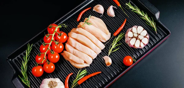 Chicken fillet in a skillet with spices and vegetables on a dark background. Raw chicken meat cut into pieces for cooking.Top view with copy space.