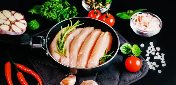 Chicken fillet in a skillet with spices and vegetables on a dark background. Raw chicken meat cut into pieces for cooking.Top view with copy space.