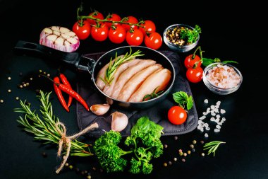 Pişirmek için kesilmiş çiğ tavuk eti. Arka planda baharat ve sebzelerle dolu tavada tavuk filetosu. Fotokopi alanı olan üst manzara..