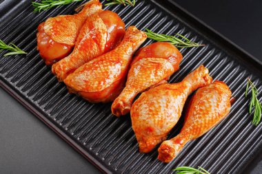 Baharatlı çiğ tavuk budu ve siyah arka planda yeşil biberiye. Izgara tavasında marine edilmiş tavuk çubuğu ve pişirmek için baharatlar..