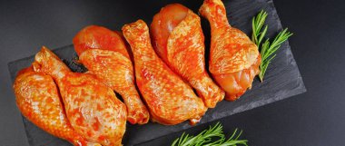 Baner. Barbekü salamura edilmiş tavuk çubukları siyah arka planda siyah bir yemek tahtasında taze biberiye yapraklarıyla birlikte. Yarı bitmiş ürün, marine edilmiş ürün, hızlı pişirme..