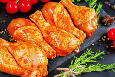 Yarı bitmiş ürün. Barbekü terbiye edilmiş tavuk dramstik üzerinde siyah bir arkaplan üzerinde taze biberiye yaprakları ve taze vişne domatesleri, yakın çekim.