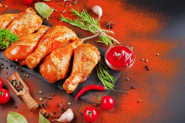 Terbiye edilmiş ürün, hızlı pişirme. Siyah bir yemek tahtasında marine edilmiş ızgara tavuk dramstik. Taze biberiye yaprakları, taze kiraz domatesleri ve çeşitli baharatlar..