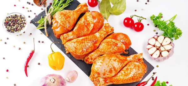 Barbekü soslu tavuk dramsticks siyah mutfak tahtası, taze biberiye yapraklı beyaz arka plan ve kiraz domatesleri, çeşitli baharatlar, yakın plan. Bir parça et. Yarı bitmiş ürün, hızlı pişirme..