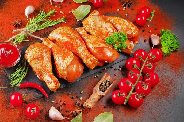 Terbiye edilmiş ürün, hızlı pişirme. Siyah bir yemek tahtasında marine edilmiş ızgara tavuk dramstik. Taze biberiye yaprakları, taze kiraz domatesleri ve çeşitli baharatlar..