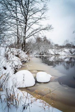 Karlı ormanlı kış manzarası, donmuş nehir ve sarı aksanlı