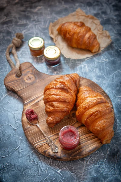 Rustic styling of fresh croissants and fruit jam on the antique wooden board